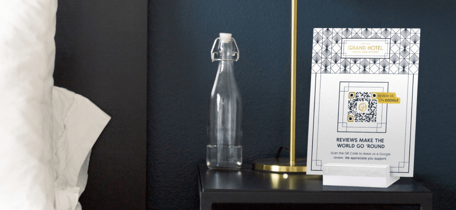 Uma cabeceira num quarto de hotel com uma garrafa de água, uma lâmpada e um display de mesa com um QR Code.